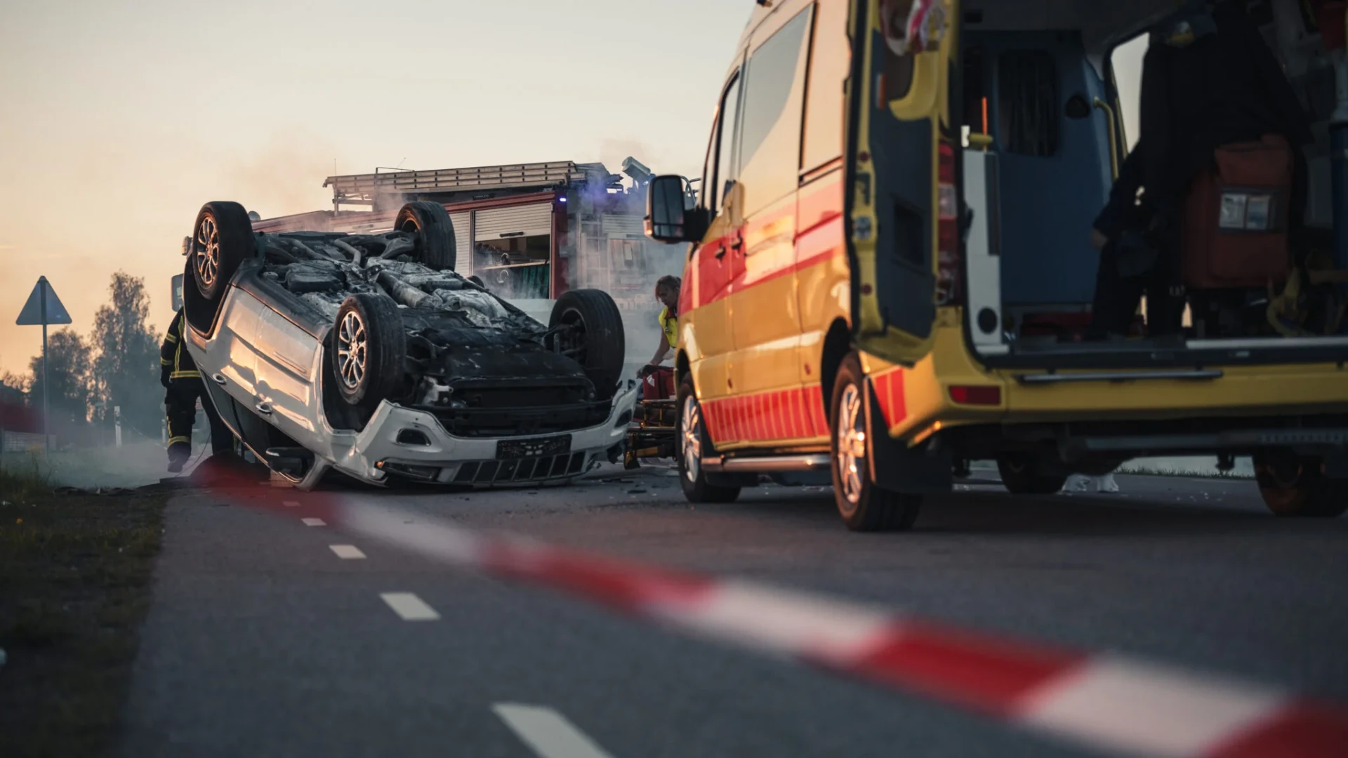 An overturned vehicle at an accident scene with an ambulance and fire engine responding